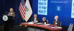 Photograph of panelist Carol Gore speaking at a podium while moderator Roger Boyd, deputy assistant secretary of HUD's Office of Native American Programs, and panelists Kevin Klingbeil and Nancy Pindus sit at a table onstage.