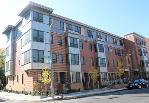 Image of a four-story residential building, lined by vegetation and sidewalks.