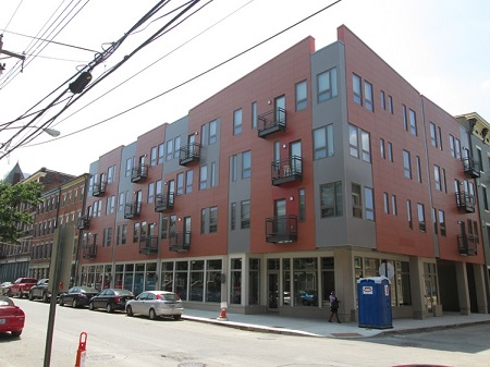 Photograph of the two street facades of a corner building, with commercial space on the first floor and residences on the upper three stories.