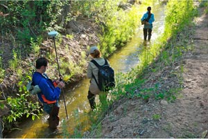 Three students walking along an acequia.