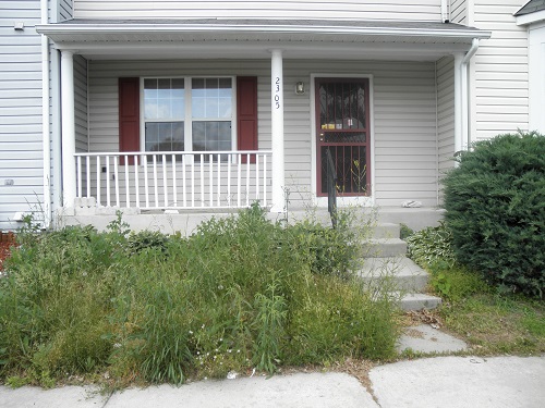 A real estate owned property with overgrown grass and no proper signage.