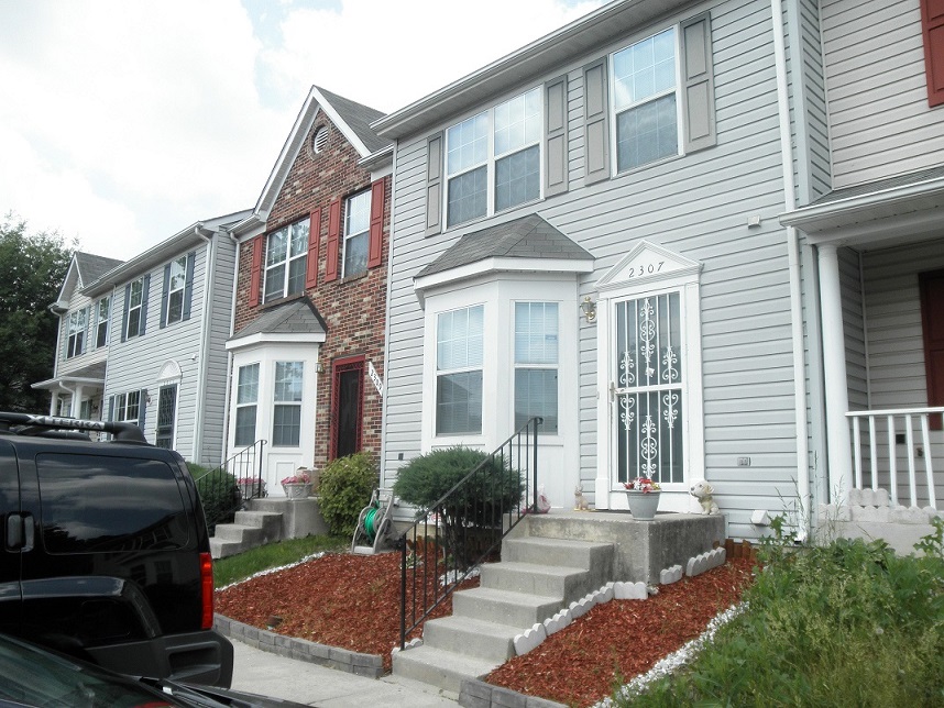 Image of residents’ well maintained front yards next to a real estate owned property, with overgrown grass.