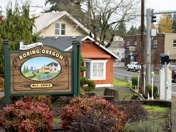 The welcome sign of Boring, Oregon, with houses and other buildings in the background.