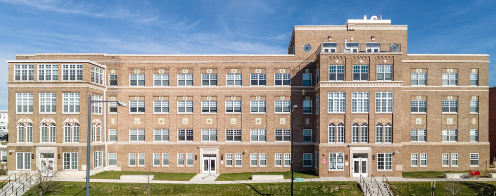 Photograph of the front of a four-story brick building with windows arranged along the length of each story.