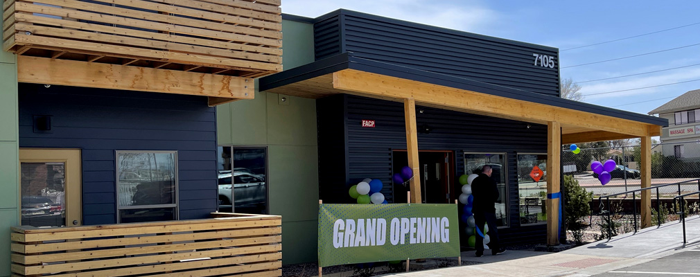 A low-rise apartment building seen from the front, with a “Grand Opening” sign and balloons.