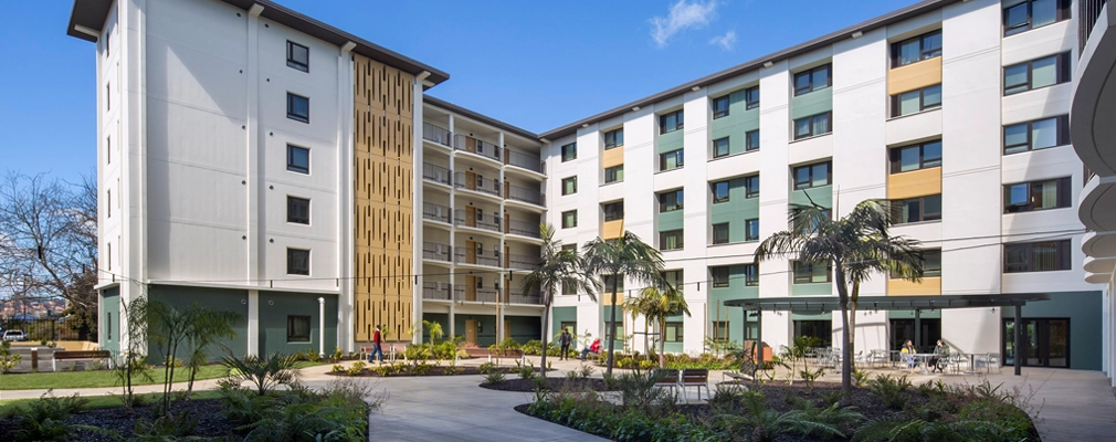 Photograph of a six-story building framing a courtyard with a mix of paved and landscaped areas.