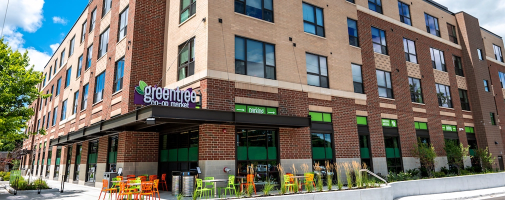 Four-story residential building with a sign for the GreenTree Co-op Market on the corner at ground level.