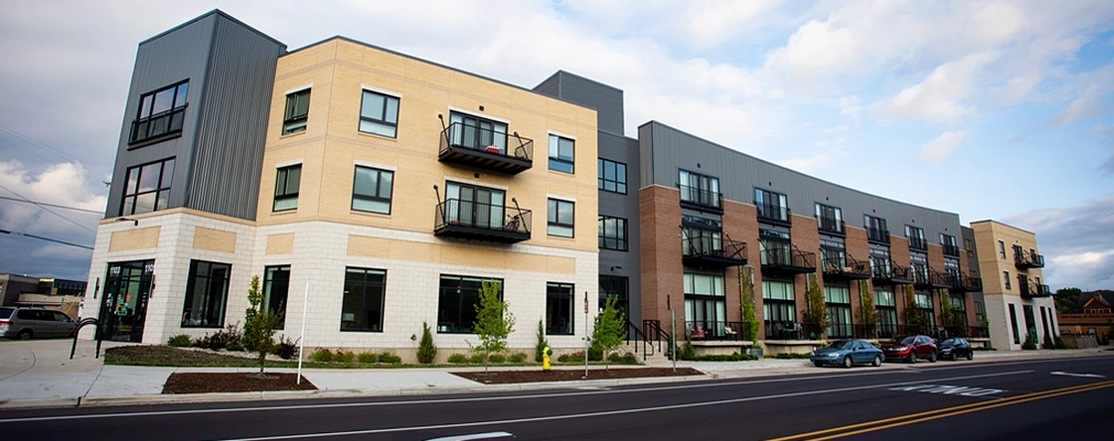 Street view of a three-story building with cars parked in the foreground.