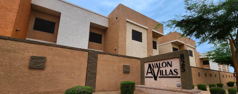 Beige- and terracotta-colored low-rise structure with plants and “Avalon Villas” sign in the foreground.