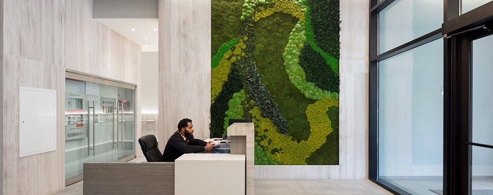 A white concrete lobby with an attended reception desk and a green wall installation.