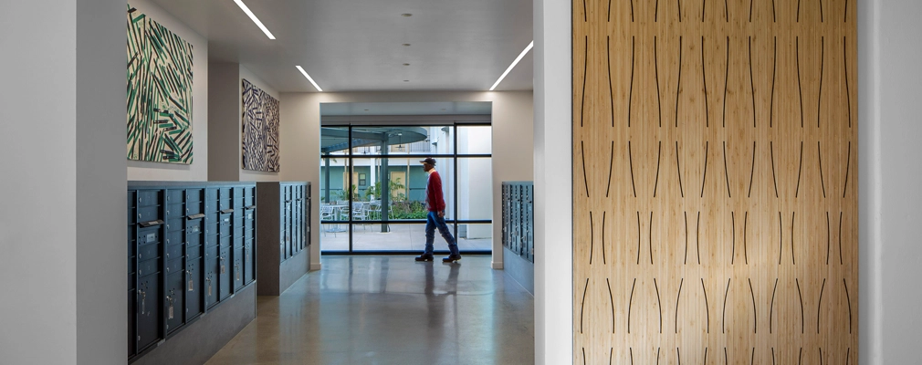 Photograph of an interior hallway with resident mailboxes along the walls and a floor-to-ceiling window at the end with a courtyard view.