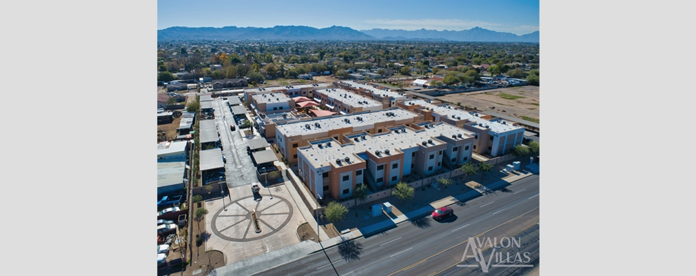 Aerial view of several adjoining low-rise apartment buildings with adjacent neighborhood and mountains in the background.