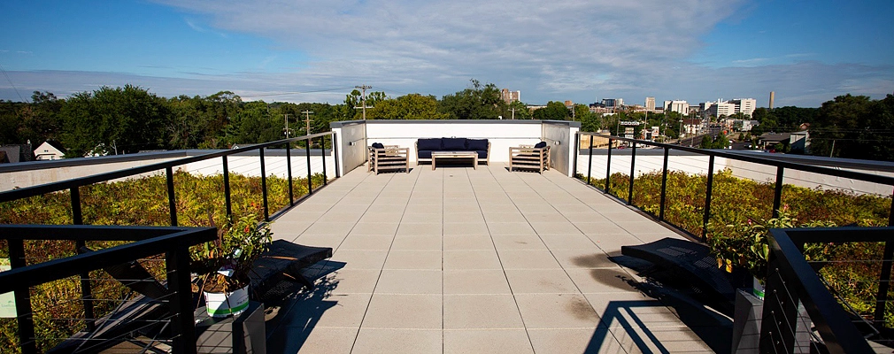 A photograph of a furnished patio flanked by vegetation on two sides and, in the background, tree canopies and a city skyline.