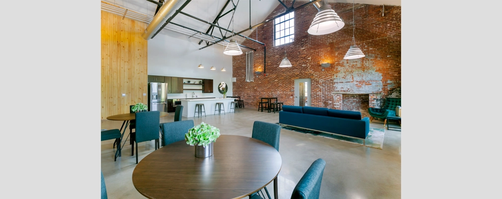 Photo of a large room with a brick fireplace, tables, chairs, a sofa, and a kitchenette.