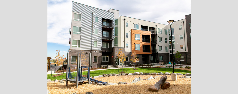 Four-story residential building with a lawn and children's play equipment in the foreground.