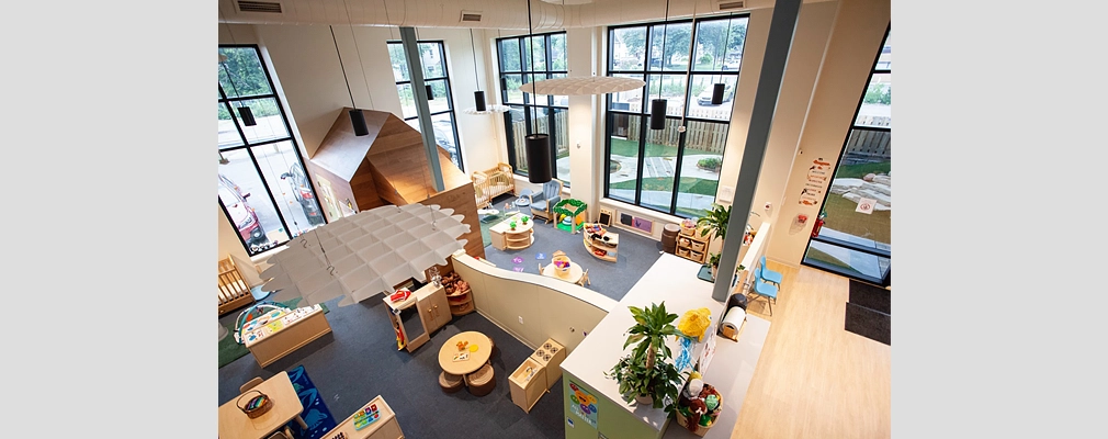 Birds-eye view of a large two-story room with multiple tall windows housing children’s play and learning areas equipped with tables, chairs and toys.