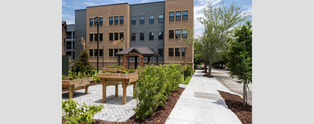 Garden with raised plant beds in front of a three-story building.