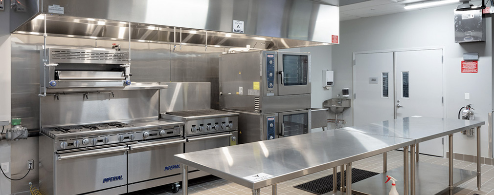 A commercial kitchen with stainless steel stovetops, ovens, and work tables.