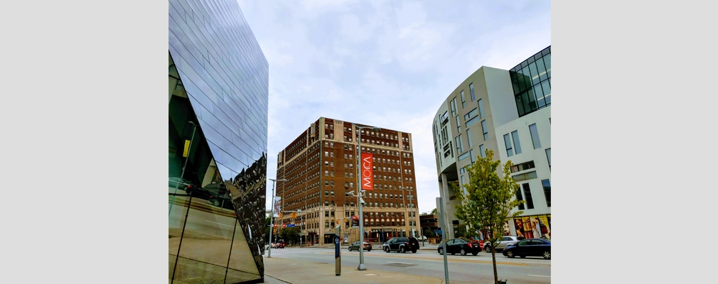 A long-range shot of a 13-story brick building on a city block near several other buildings.