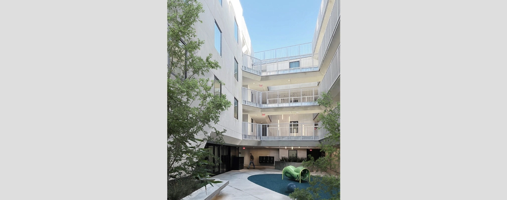 Courtyard of a four-story residential building with landscaping and play equipment.