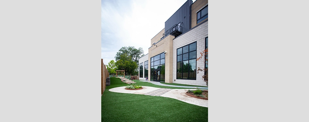 A perspective photograph of a landscaped green space abutting a building and, in the background, steps leading to an archway.