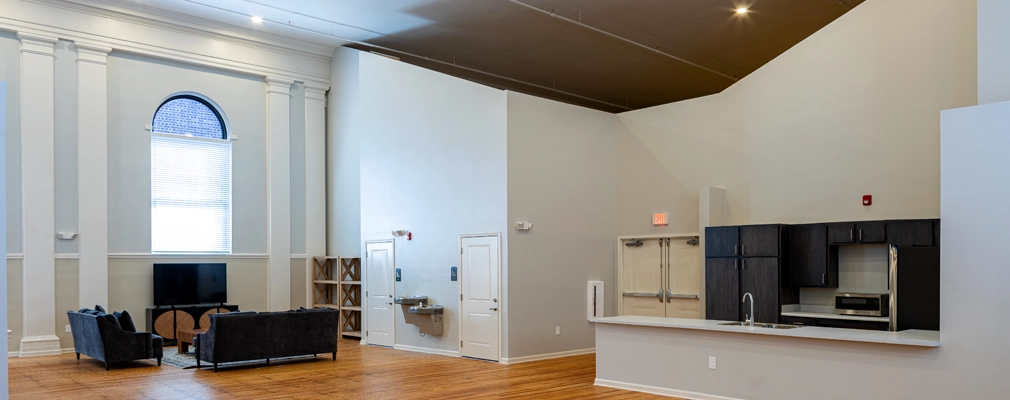 Wood-floored community room with seating area and kitchen with counter and cabinets.