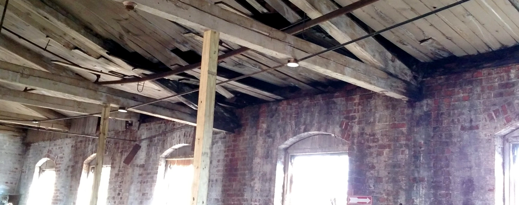 Photo of a dilapidated wooden ceiling from the inside of a brick building.