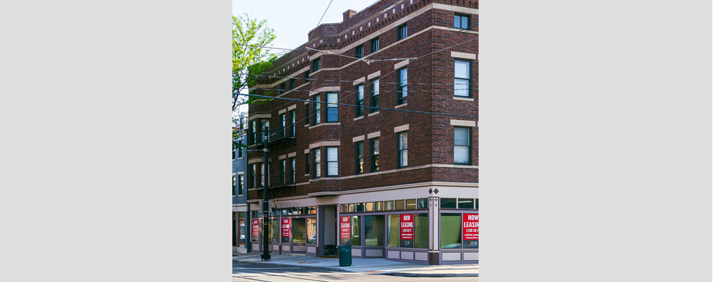 Exterior of historic, four-story apartment building with ground-level retail spaces for lease.