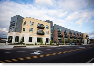 Street view of a three-story building with cars parked in the foreground.