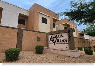 Beige- and terracotta-colored low-rise structure with plants and “Avalon Villas” sign in the foreground.