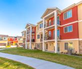 Exterior view of townhomes with porches and balconies. A pathway and grass covered ground are in front of the houses.