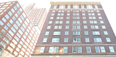 Brick facade of a 13-story building attached to a 3-story building and surrounded by multiple buildings of various heights.