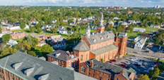 Aerial view of a three-story brick building with a church and single-family homes in the background.