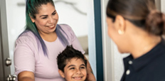 A Hispanic mother and her son receive a package delivered by another woman at the door.