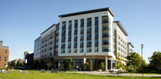 Multistory buildings in the background and a grassy park and picnic benches in the foreground.