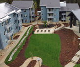 An interior courtyard with an open lawn and a patio surrounded by two 3-story buildings and a one-story building.