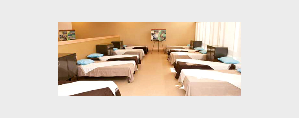 Photograph of 10 beds arranged in 2 rows in a large room.