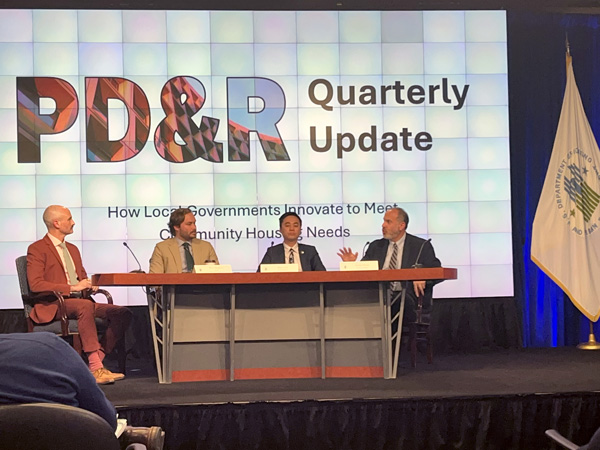 Four panelists sit in front of a large screen that reads "PD&R Quarterly Update: How Local Governments Innovate to Meet Community Housing Needs."