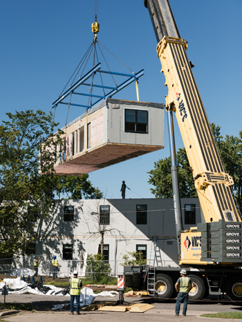 A modular housing section being lowered into place by a crane.
