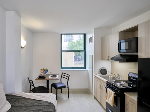 Interior of studio apartment with a bed, table with chairs, kitchen, and window.