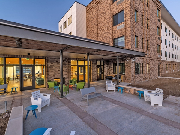 An indoor/outdoor gathering space with tables and chairs, adjacent to an apartment building. 