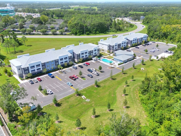 Aerial view of two 3-story buildings with a pool and a low-rise building centered in the parking lot.