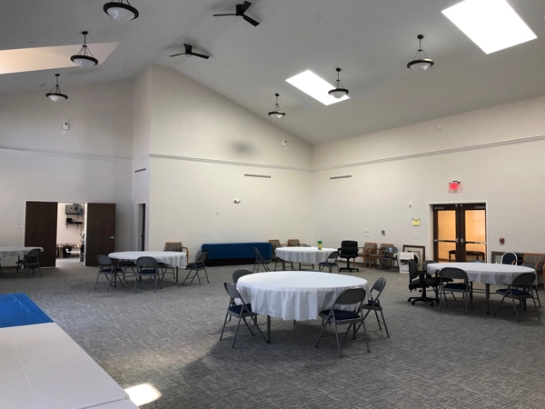 A large room with high ceilings, white walls, and gray carpeting. Several tables and folding chairs are set up in the room.