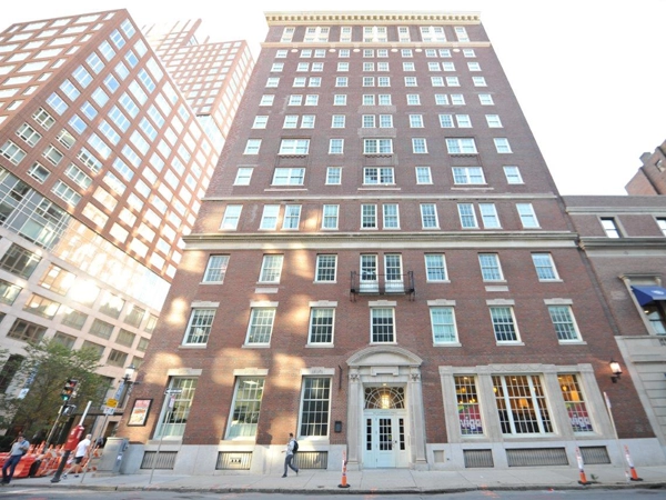 Brick facade of a 13-story building attached to a 3-story building and surrounded by multiple buildings of various heights.