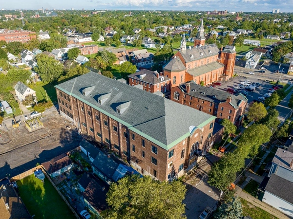 Aerial view of a three-story brick building with a church and single-family homes in the background.