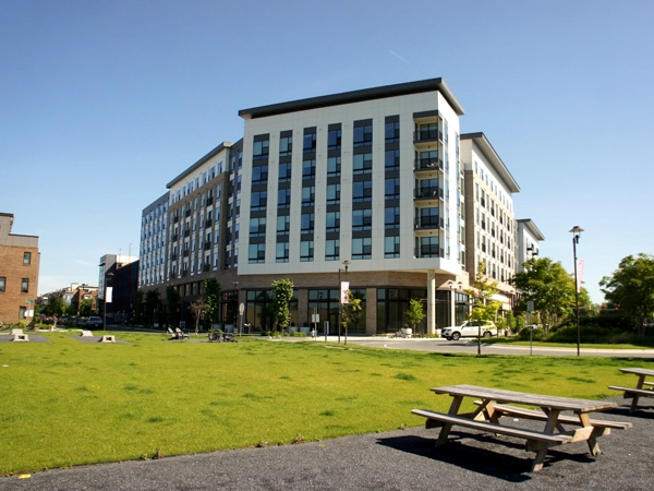 Multistory buildings in the background and a grassy park and picnic benches in the foreground.