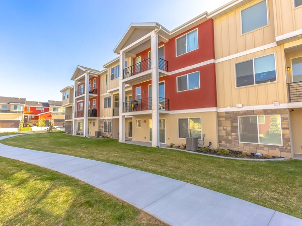 Exterior view of townhomes with porches and balconies. A pathway and grass covered ground are in front of the houses.